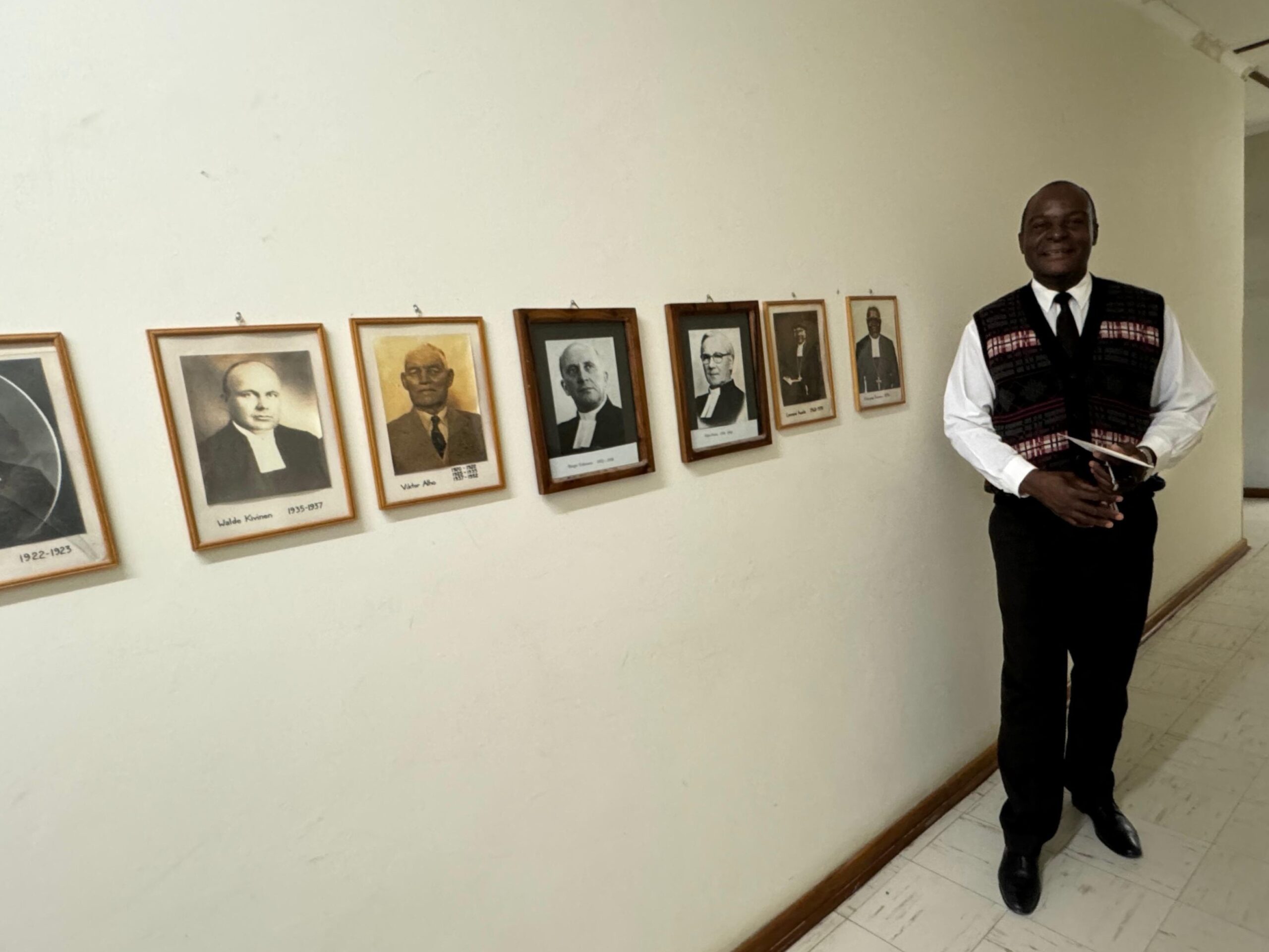 Namibian kirkon pääsihteeri Johannes Haufiku esittelee kirkon johtajien kuvakavalkaadia.
