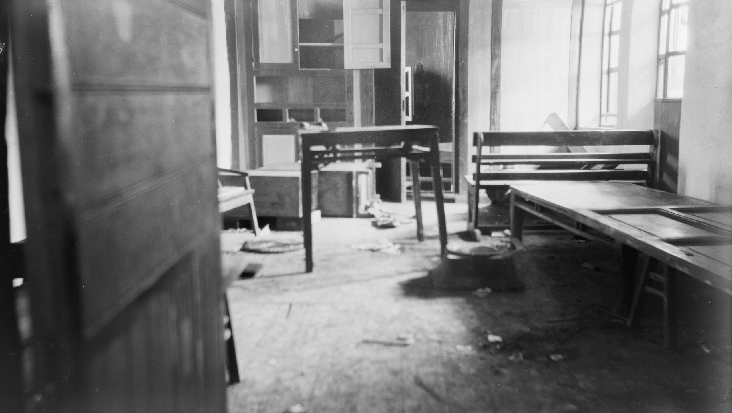Mustavalkoinen valokuva huoneesta, jossa huonekalut on hujanhajan ja keittiönkaapin ovet levällään.